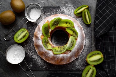 Photo of Homemade yogurt cake with kiwi and powdered sugar on black table, flat lay