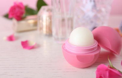 Photo of Lip balm and flowers on white wooden table, closeup