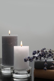 Wax candles in glass holders near books and lavender flowers on table against light background