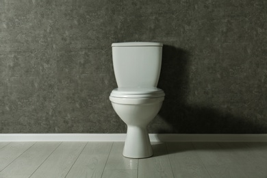 Photo of New toilet bowl near grey wall indoors