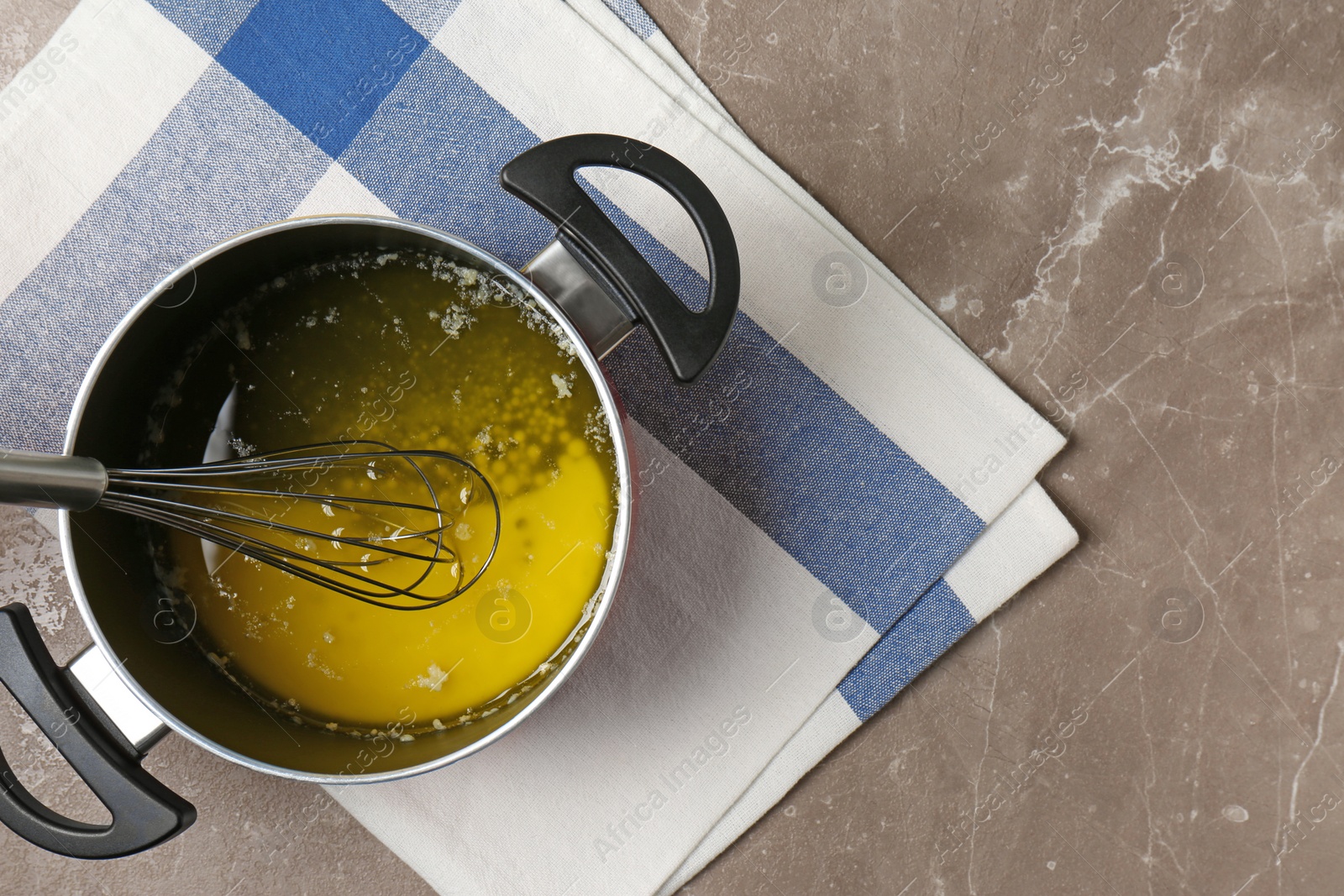 Photo of Pot with melting butter and whisk on grey table, top view. Space for text