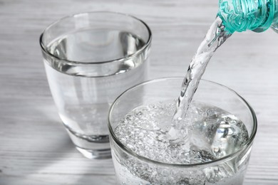 Pouring soda water from bottle into glass on white wooden table, closeup