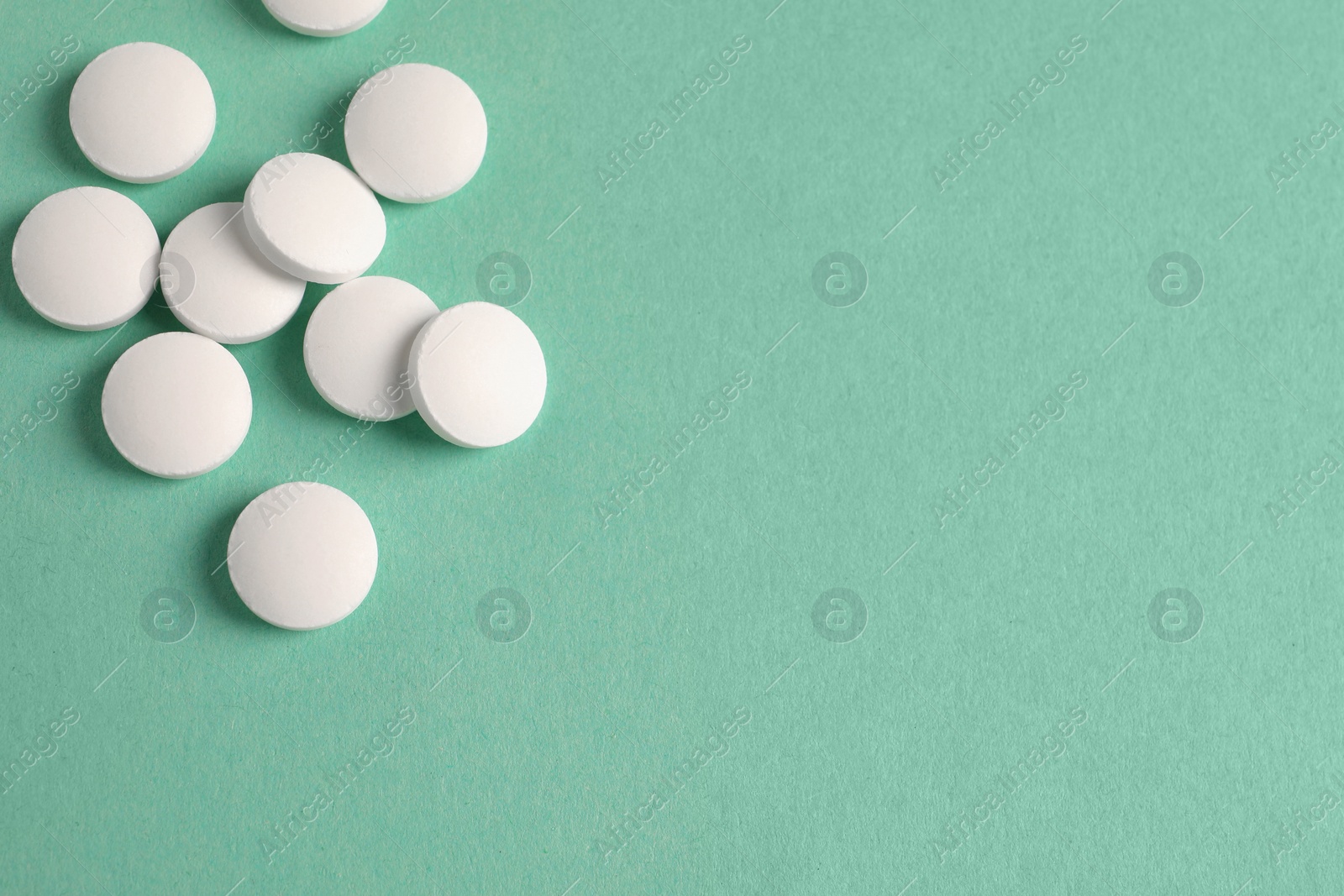 Photo of Pile of white pills on green background, flat lay. Space for text