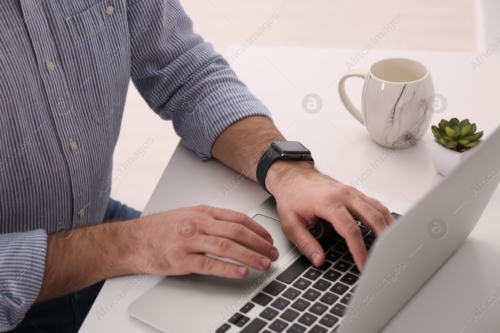 Photo of Young man with smart watch working on laptop at table in office, closeup