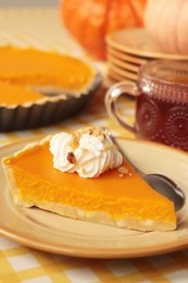 Photo of Piece of fresh homemade pumpkin pie served with whipped cream and tea on table, closeup