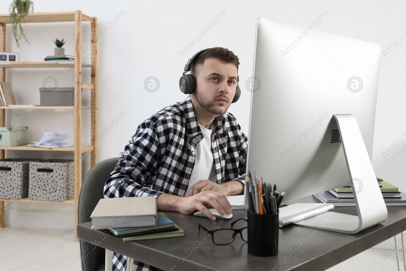 Photo of Young man in headphones using modern computer for studying at home. Distance learning