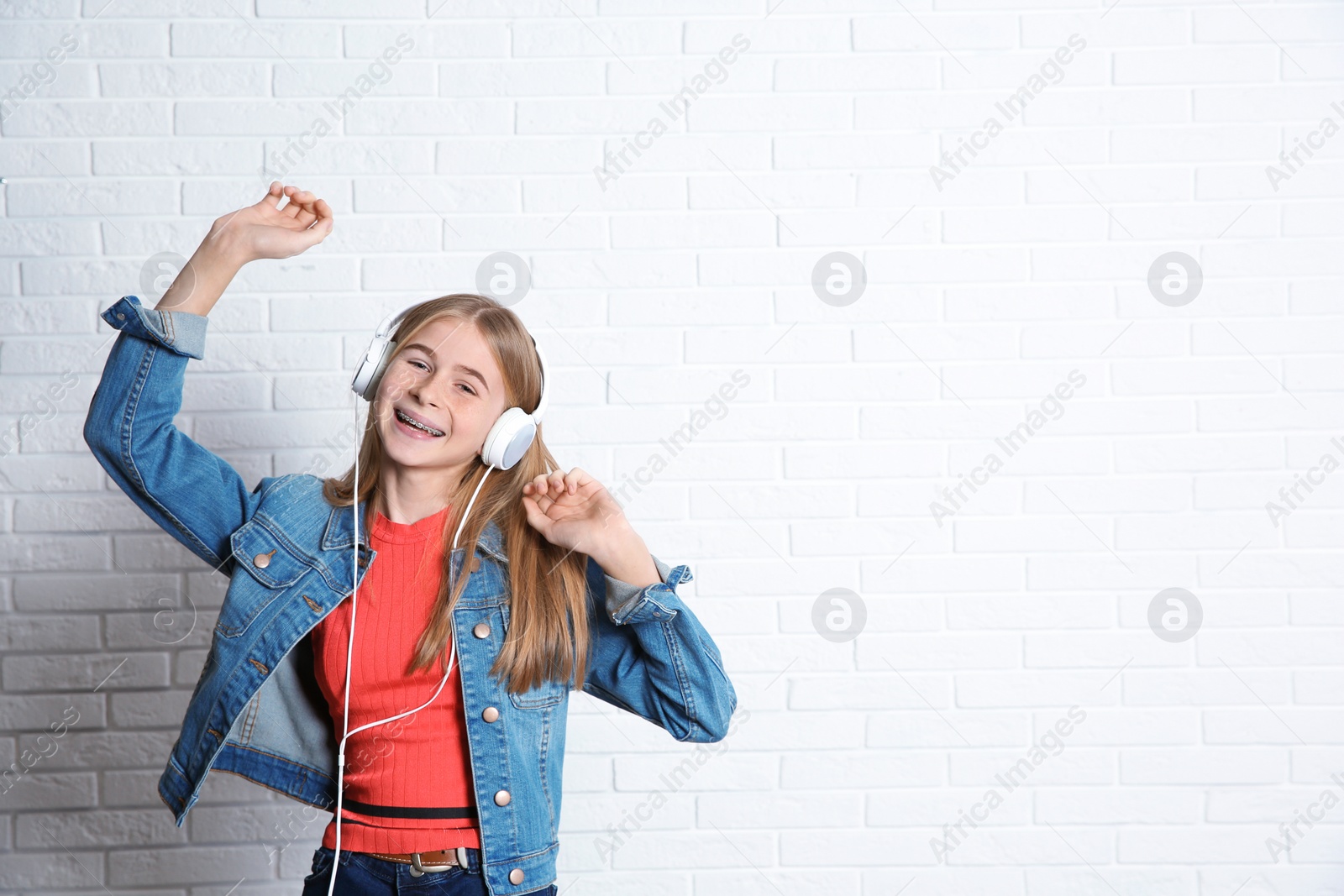 Photo of Teen girl listening to music with headphones near brick wall. Space for text