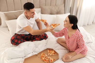 Happy couple in pyjamas eating pizza on bed at home