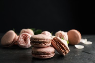 Photo of Delicious macarons and flowers on black table