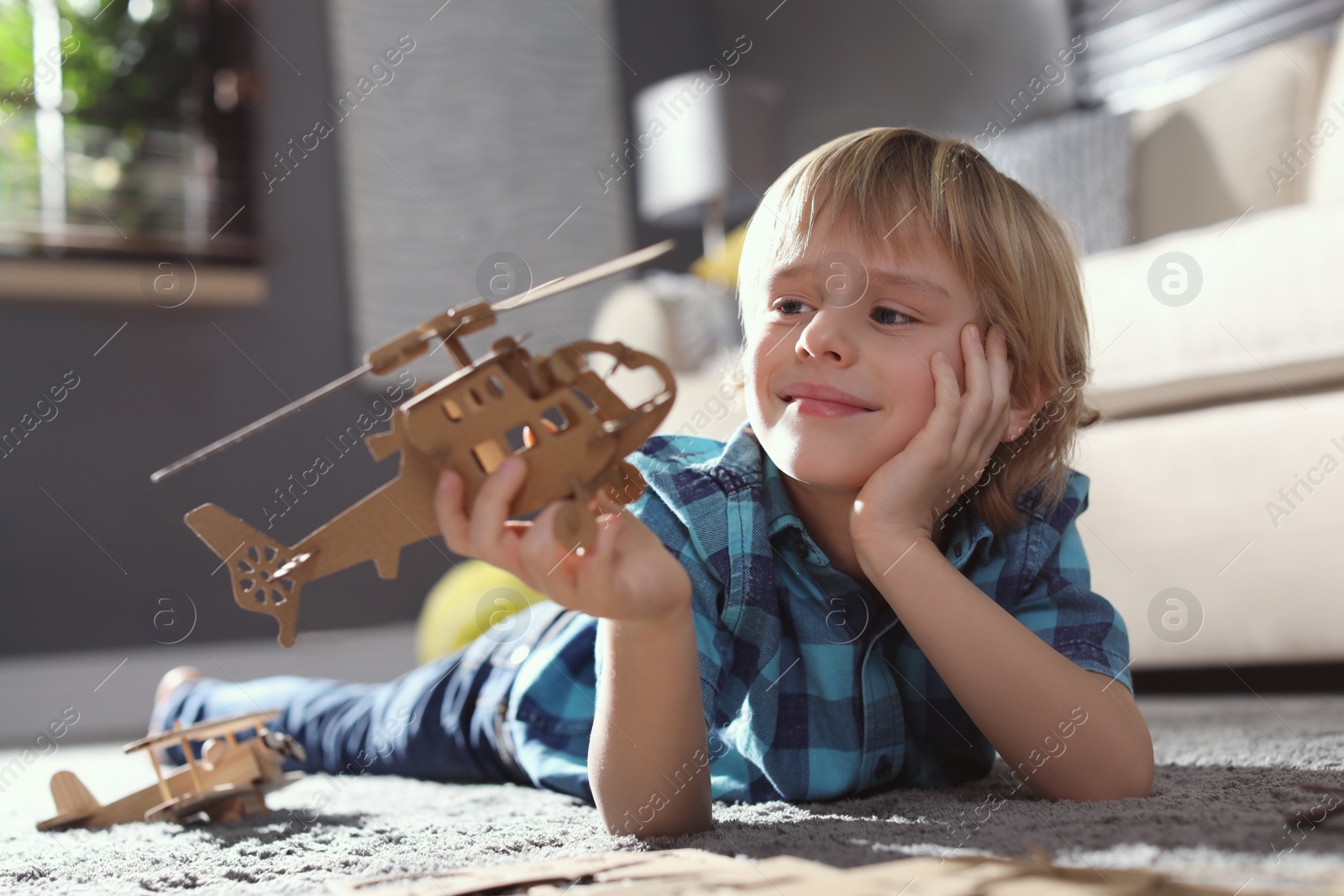 Photo of Little boy playing with cardboard helicopter on floor at home. Creative hobby