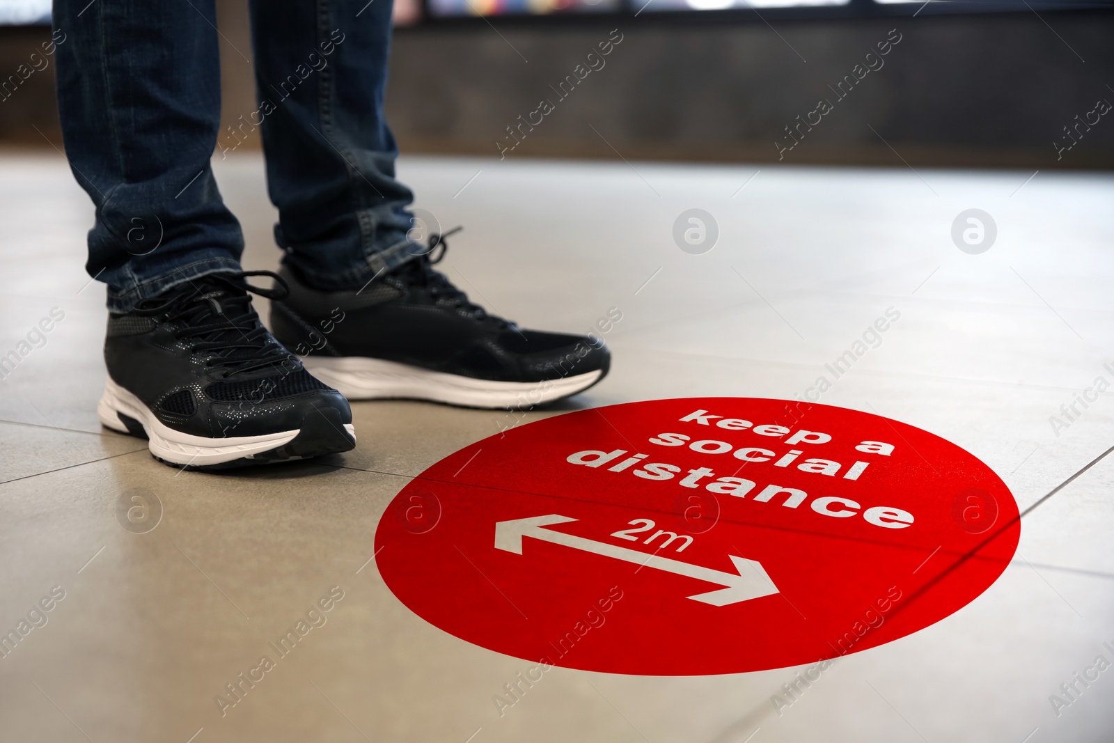 Image of Keep social distance as preventive measure during coronavirus outbreak. Red warning sign on floor in front of man, closeup