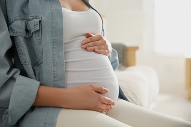 Photo of Pregnant woman touching her belly indoors, closeup