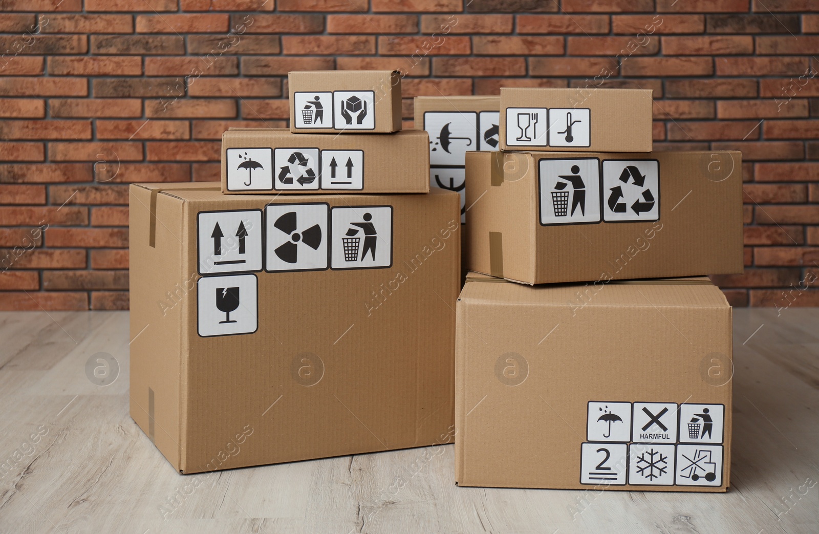 Photo of Cardboard boxes with different packaging symbols on floor near brick wall. Parcel delivery