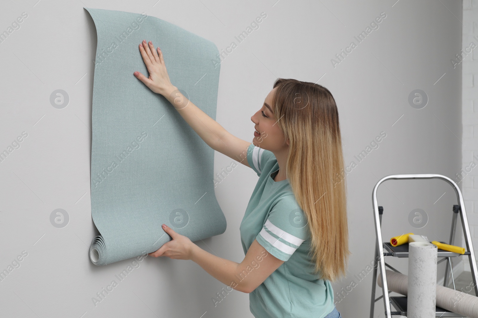 Photo of Woman hanging stylish wall paper sheet indoors