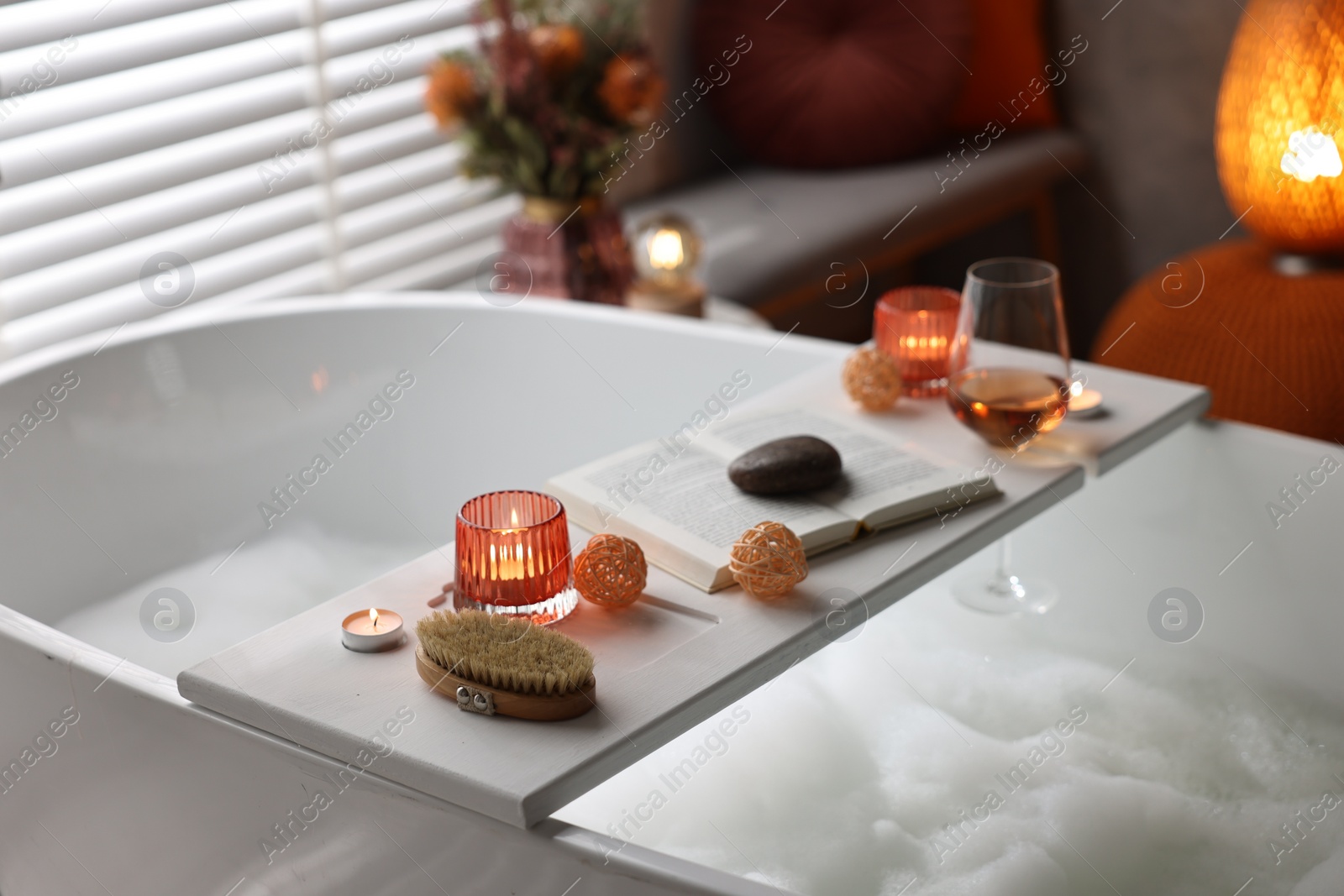 Photo of White wooden tray with burning candles and brush on bathtub in bathroom