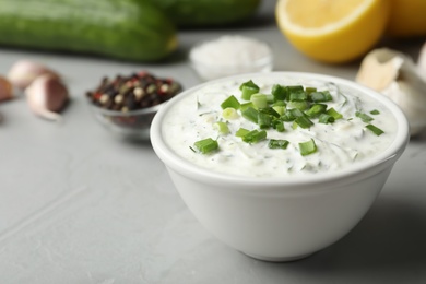 Photo of Bowl with cucumber sauce on grey background. Space for text