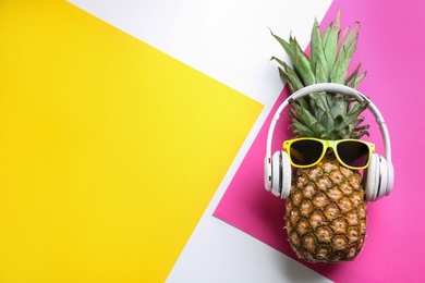 Photo of Top view of pineapple with headphones and sunglasses on color background, space for text. Creative concept