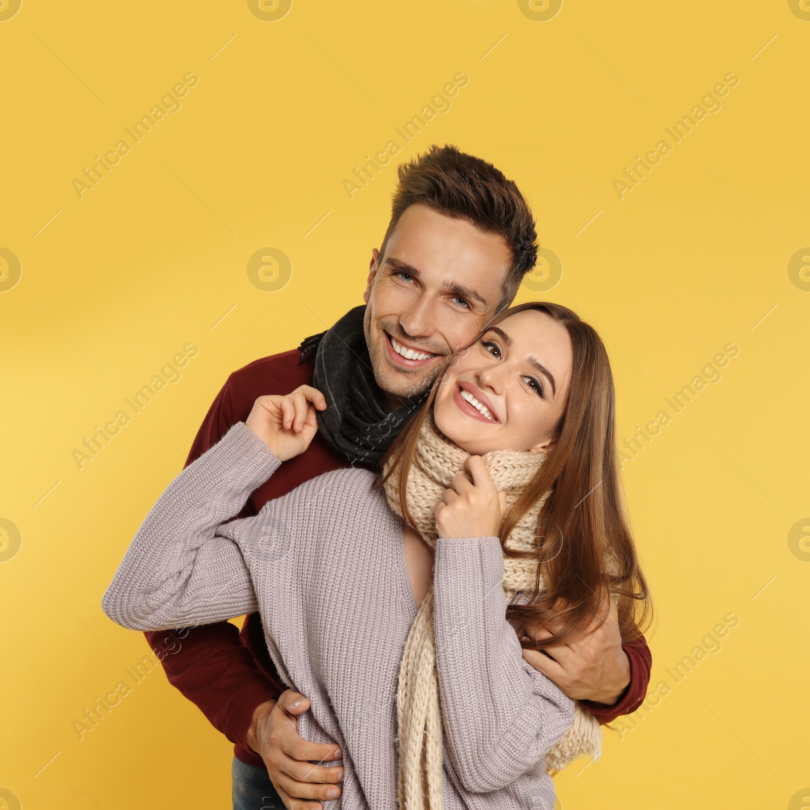 Photo of Happy young couple in warm clothes on yellow background. Winter season