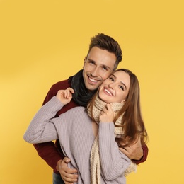 Photo of Happy young couple in warm clothes on yellow background. Winter season