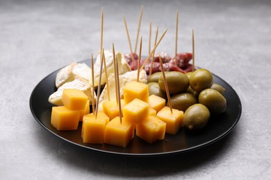 Photo of Toothpick appetizers. Pieces of cheese, sausage and olives on light grey table