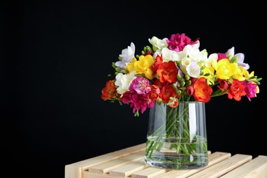 Photo of Bouquet of spring freesia flowers in vase on dark background. Space for text