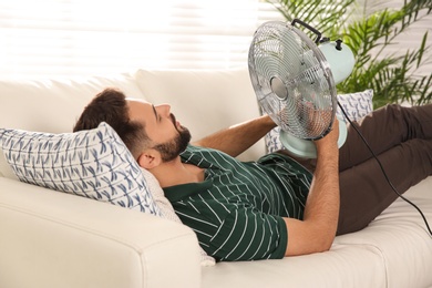 Photo of Man with fan lying on sofa home. Summer heat