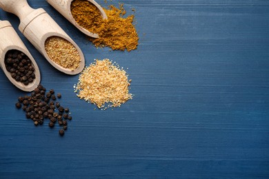 Photo of Wooden scoops with different spices on blue table, flat lay. Space for text