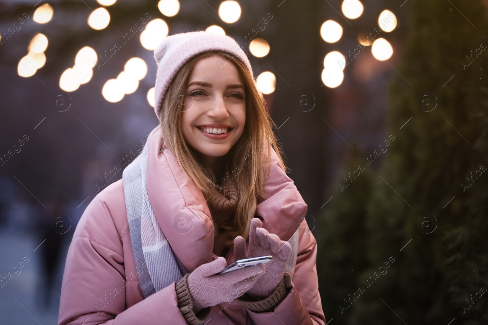 Photo of Happy young woman with mobile phone on city street in evening. Christmas celebration