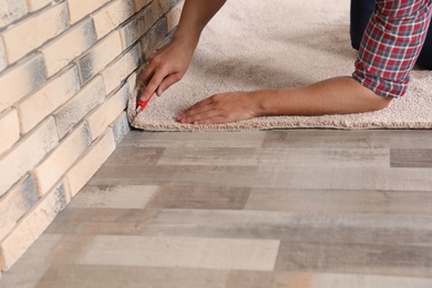 Photo of Man cutting new carpet flooring indoors, closeup. Space for text