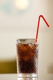 Photo of Glass of cola with ice on table against blurred background