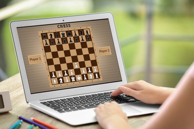 Image of Woman playing online chess on laptop at table, closeup
