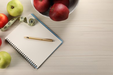 Photo of Healthy diet. Fresh apples, measuring tape, notebook and pen on light wooden table, flat lay. Space for text