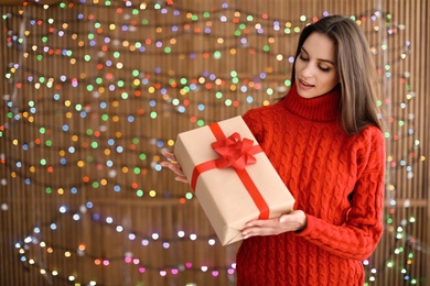 Photo of Beautiful young woman with Christmas gift on blurred lights background