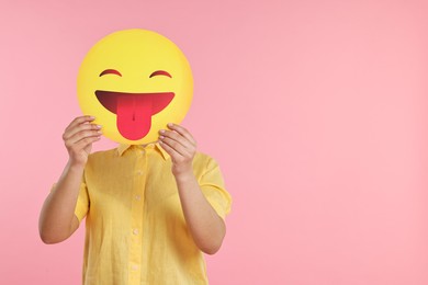 Photo of Woman covering face with emoticon sticking out tongue on pink background. Space for text