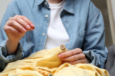 Photo of Woman sewing button with needle and thread onto shirt at home, closeup