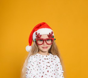 Girl wearing red decorative eyeglasses and Santa hat on orange background
