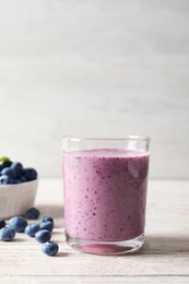 Tasty blueberry smoothie in glass and bowl with fresh berries on table