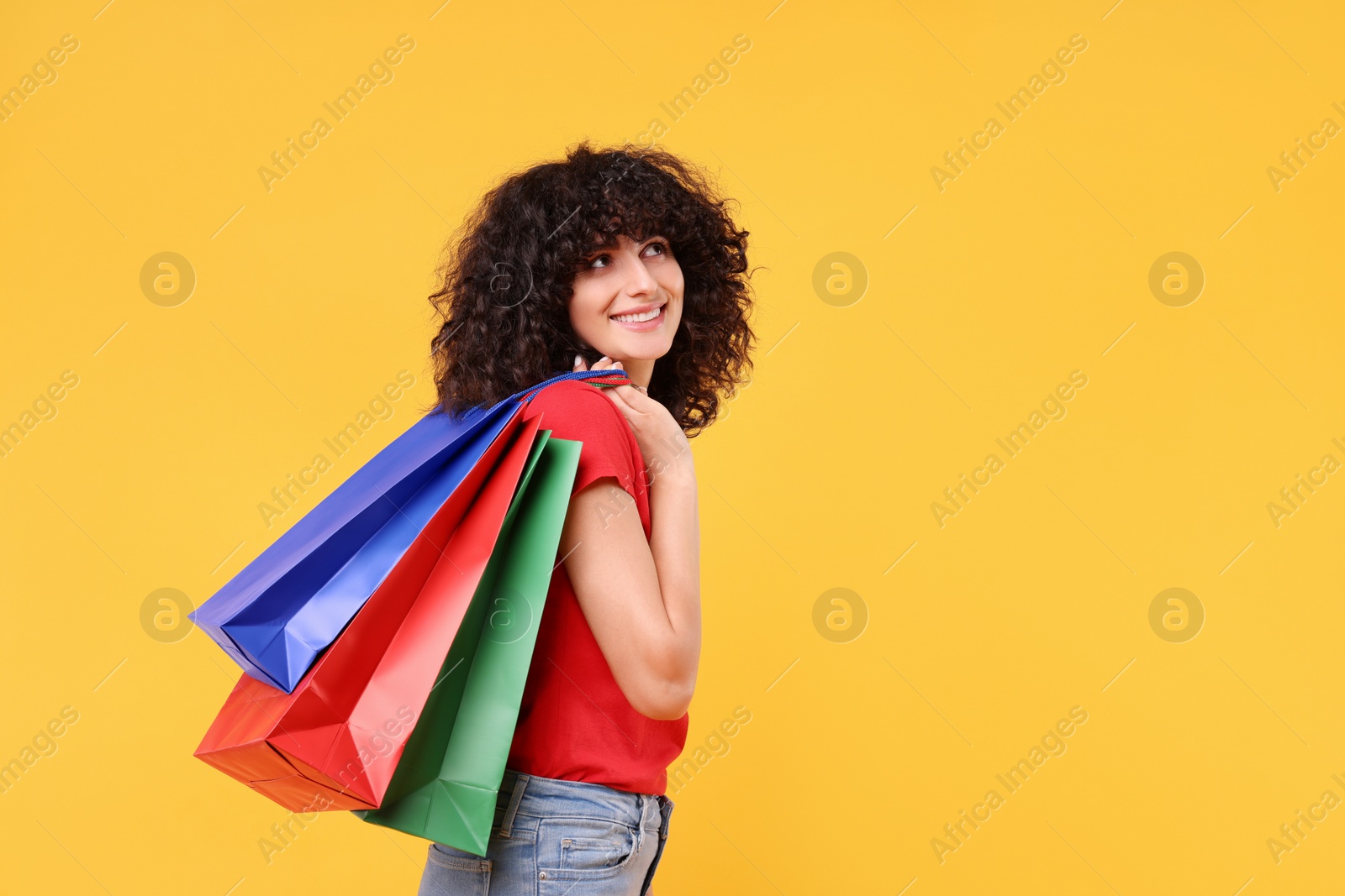 Photo of Happy young woman with shopping bags on yellow background. Space for text