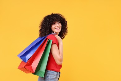 Happy young woman with shopping bags on yellow background. Space for text