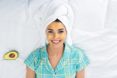 Photo of Young woman with facial mask lying on bed, top view