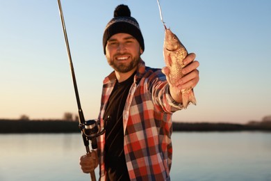 Photo of Fisherman with rod and catch at riverside, focus on fish