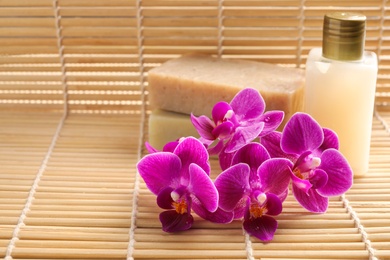 Photo of Beautiful orchid flowers and soap on bamboo mat, space for text