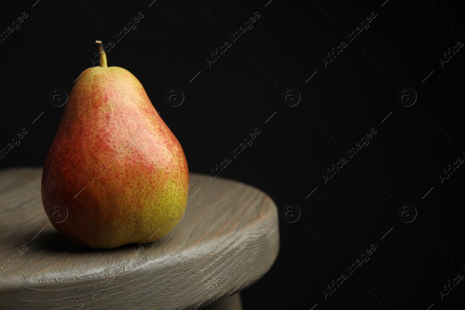 Photo of Ripe juicy pear on brown wooden table against black background. Space for text