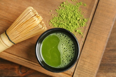 Photo of Chawan with fresh matcha tea and chasen on wooden board, top view