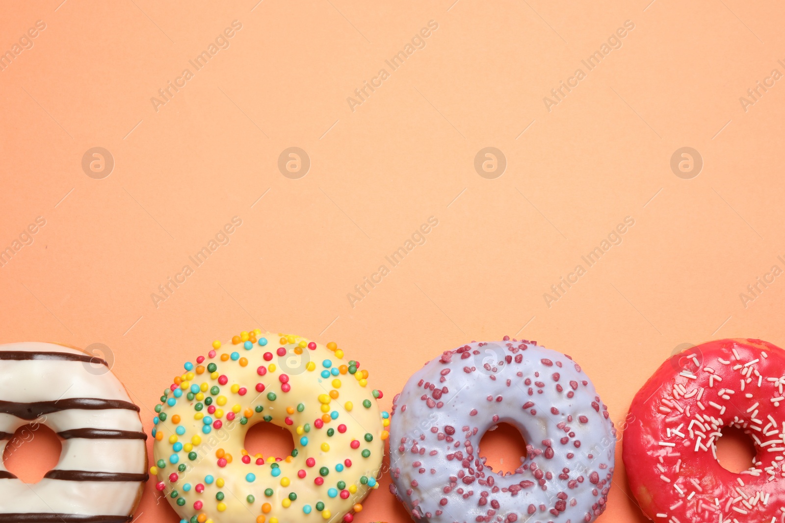 Photo of Delicious glazed donuts on orange background, flat lay. Space for text