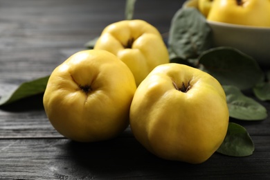 Photo of Fresh ripe organic quinces with leaves on black wooden table, closeup