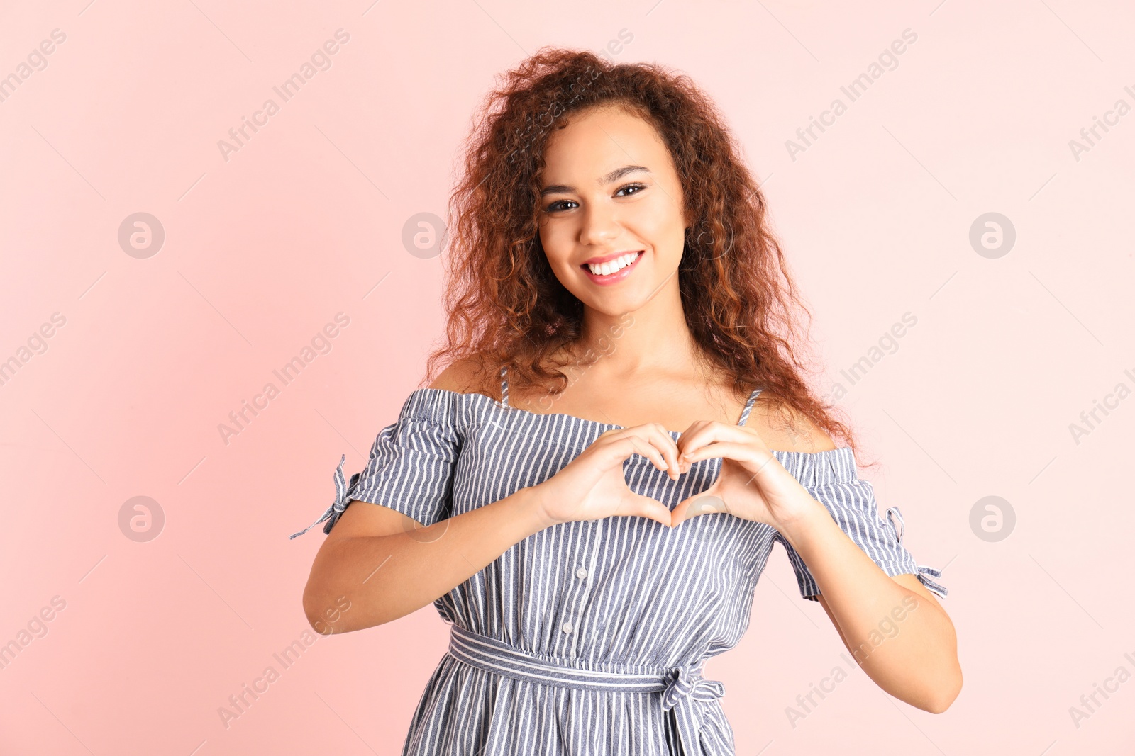 Photo of African-American woman making heart with her hands on color background