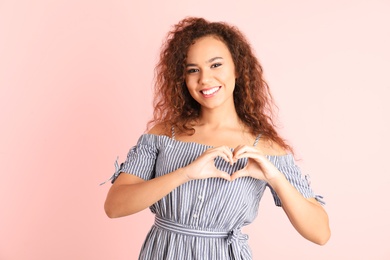 Photo of African-American woman making heart with her hands on color background
