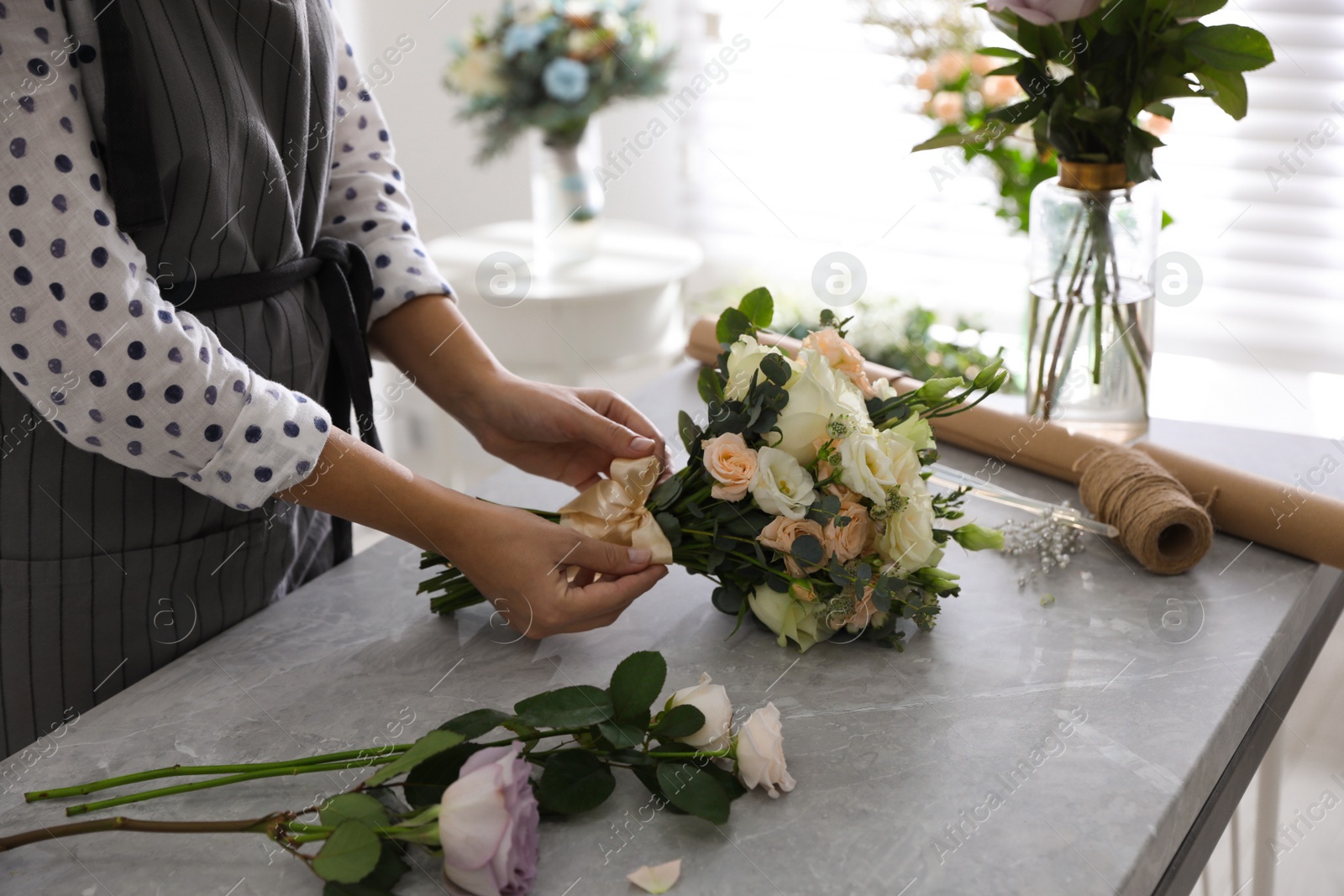 Photo of Florist tieing bow of beautiful wedding bouquet at light grey marble table, closeup