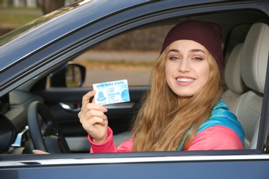 Happy woman holding driving license in car